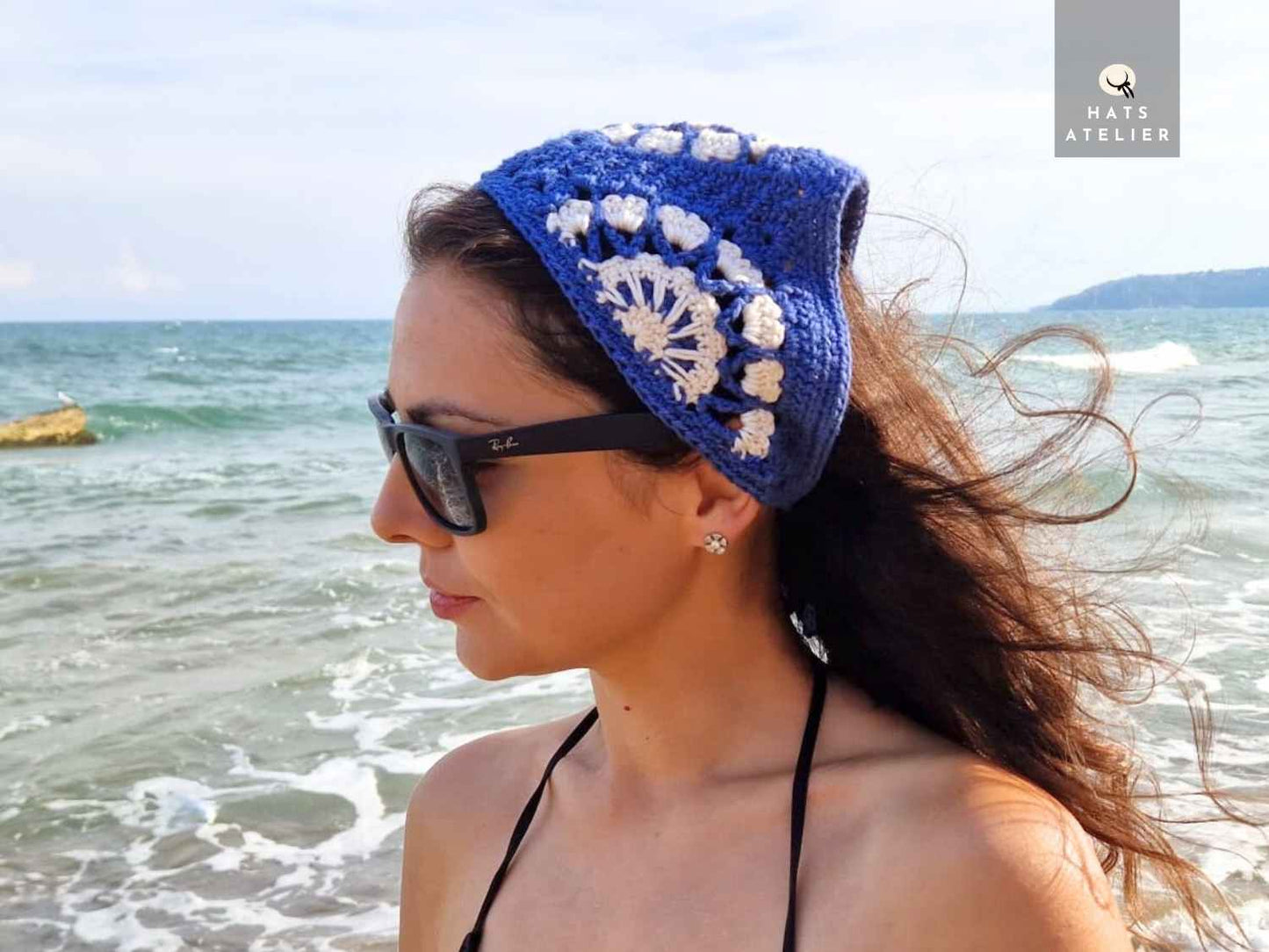 Woman wearing a blue crochet headband with white flowers at the beach.