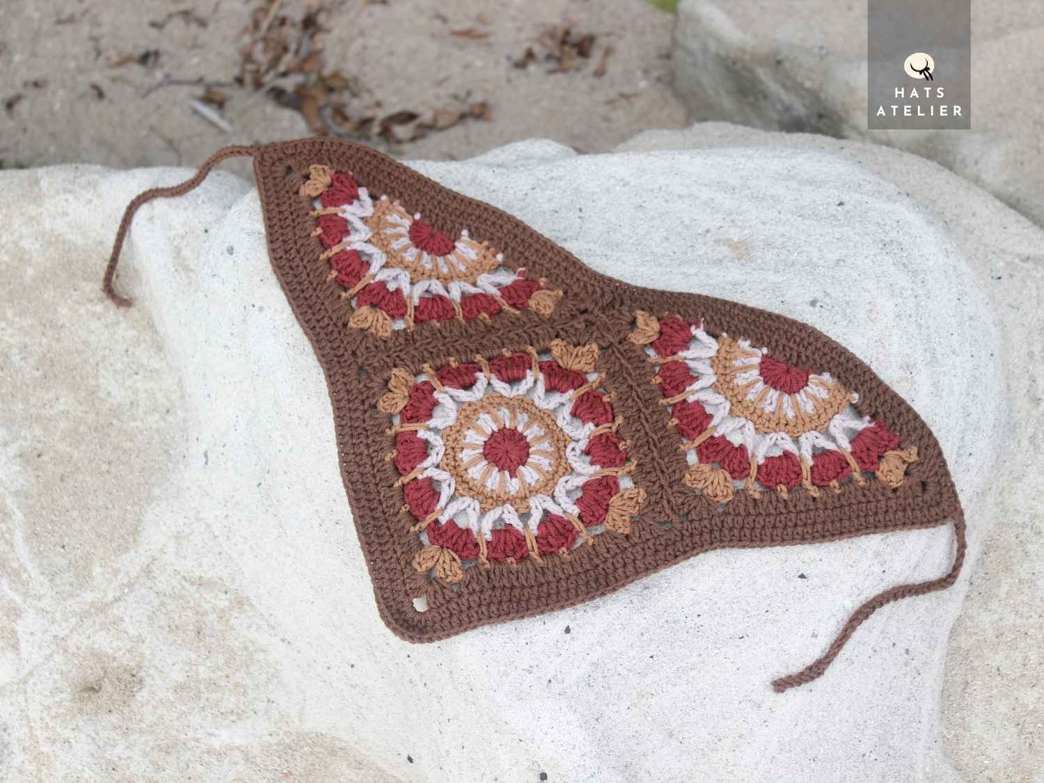 Crocheted heart-shaped blanket with floral patterns on a stone surface, featuring the brand 'Hats Atelier'.