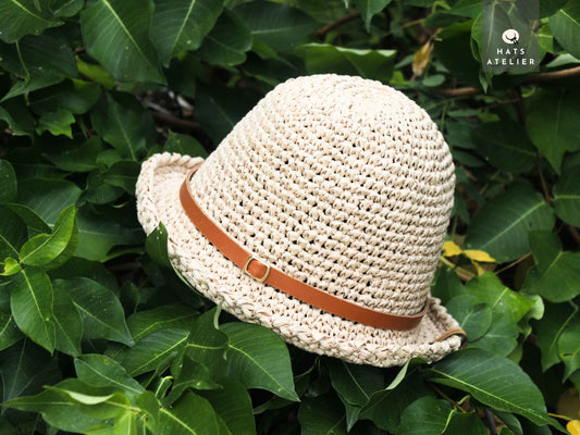 Natural crochet raffia hat with medium brim and leather band on green foliage background