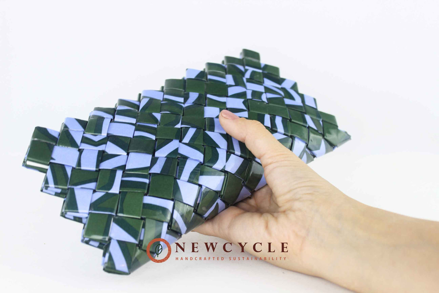 Hand showing the angled view of the handmade upcycled woven clutch in forest green and powder blue.