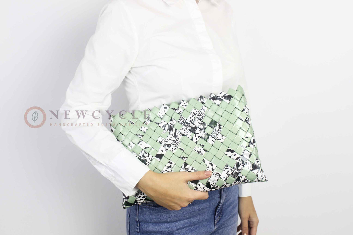 Oversized green woven clutch with black-and-white animal print shown in hand