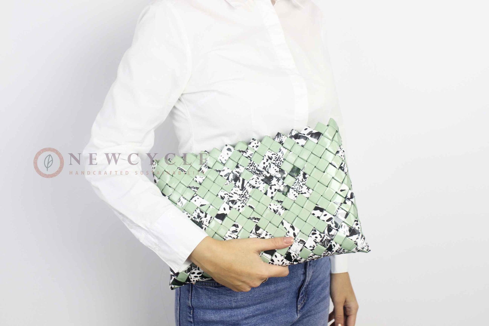 Oversized green woven clutch with black-and-white animal print shown in hand