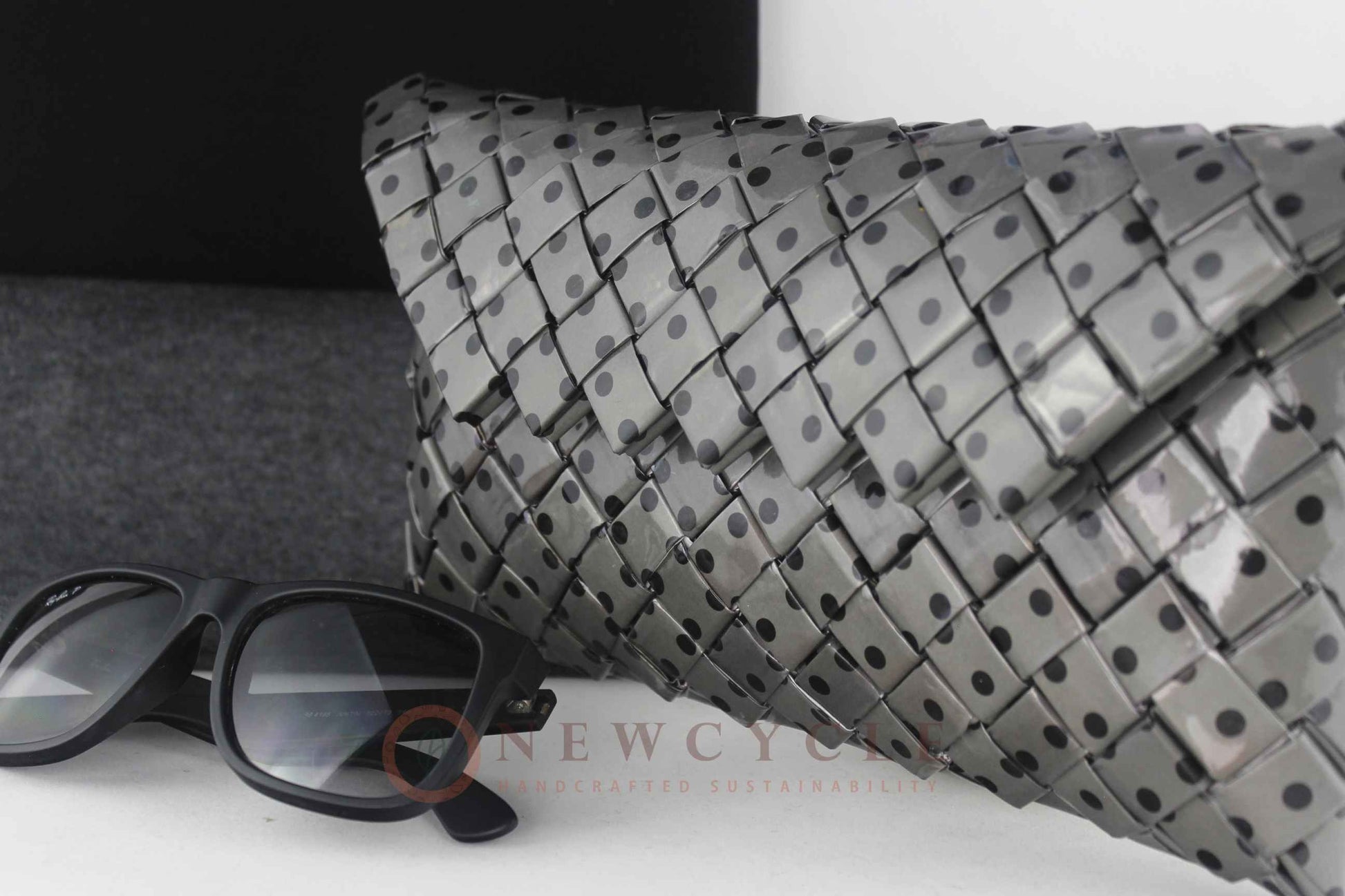 Black and grey polka-dot woven clutch displayed on a minimal background