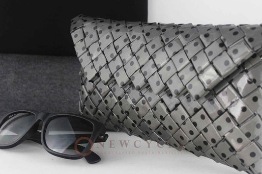 Black and grey polka-dot woven clutch displayed on a minimal background