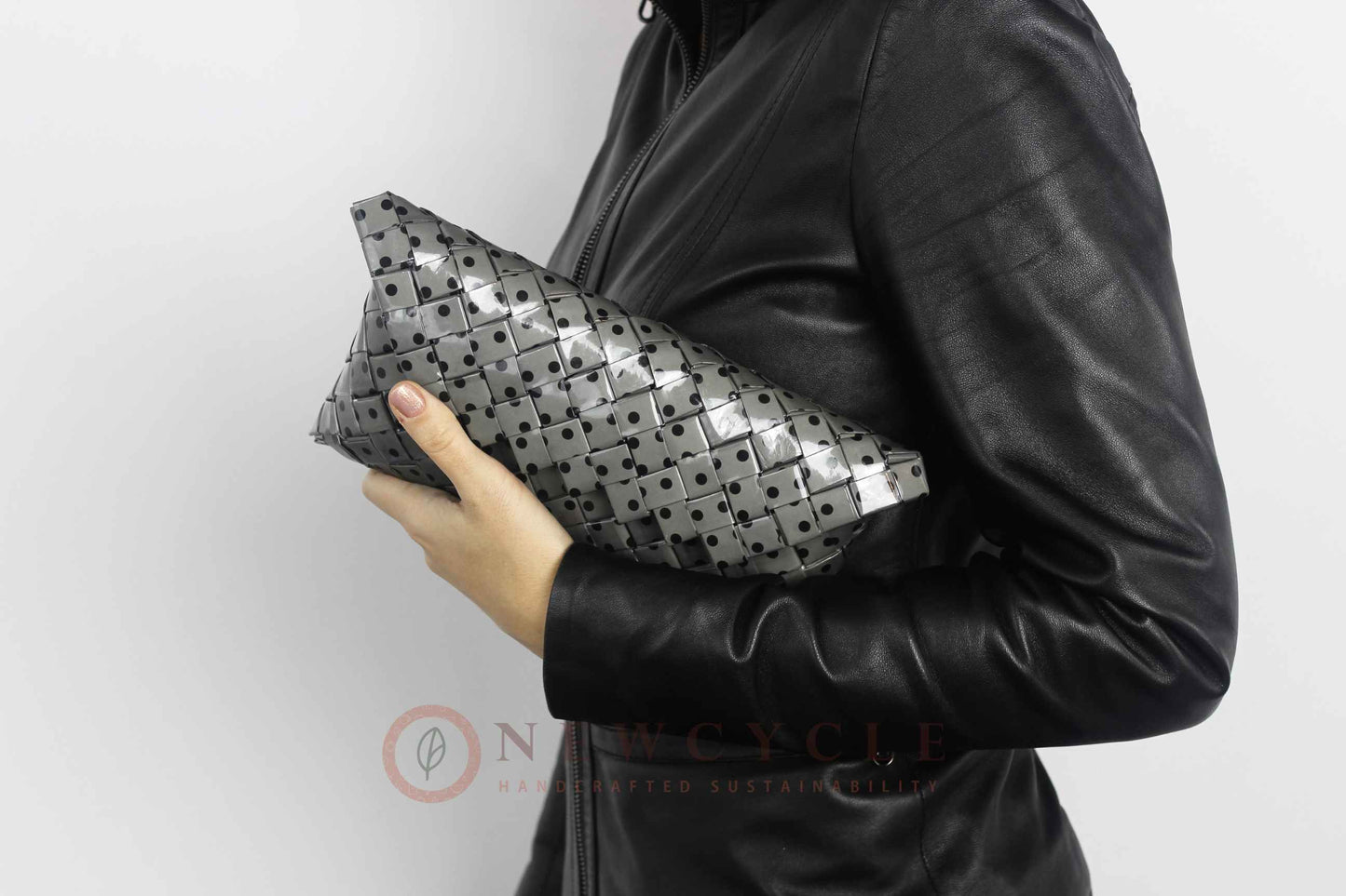 Black and grey polka-dot woven purse held in hand with a leather jacket outfit