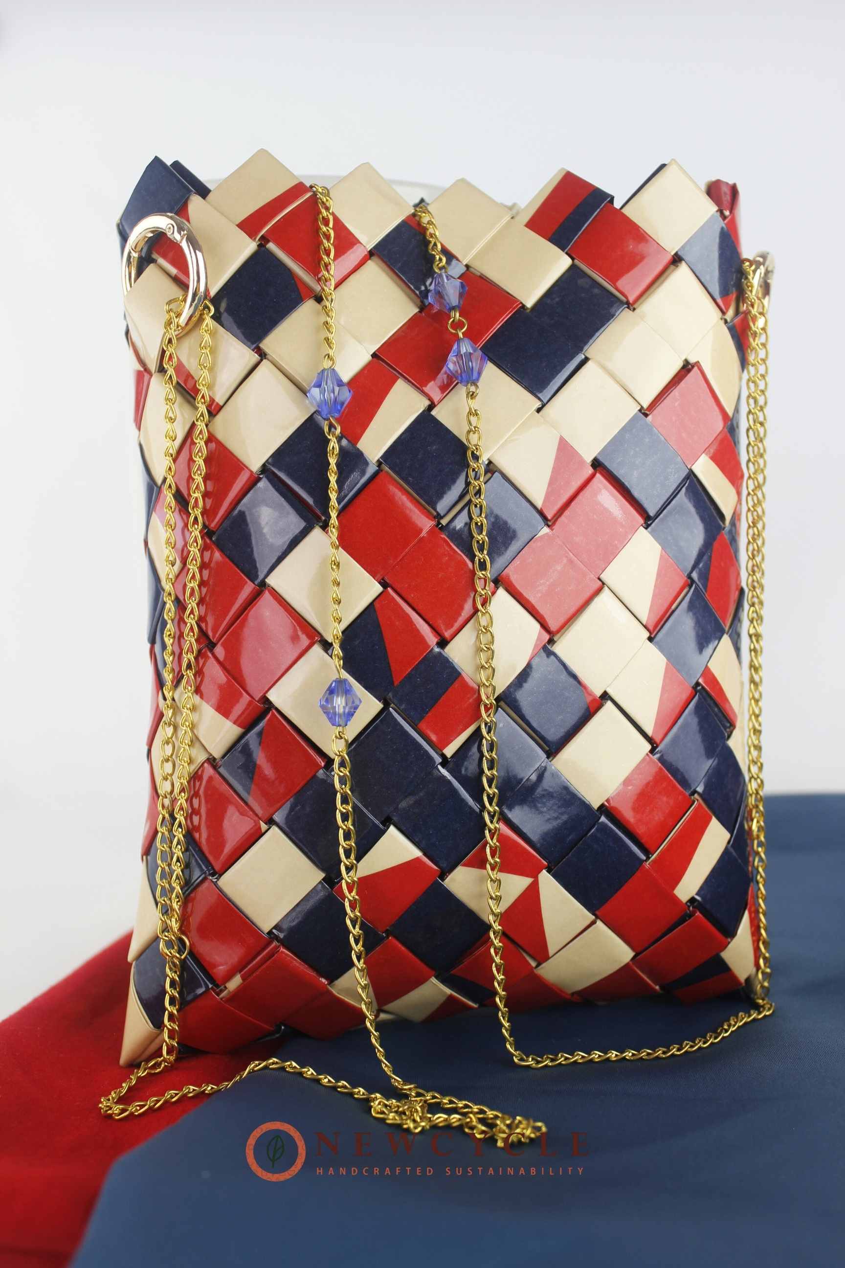 Red navy beige woven bag standing upright with gold chain and beads